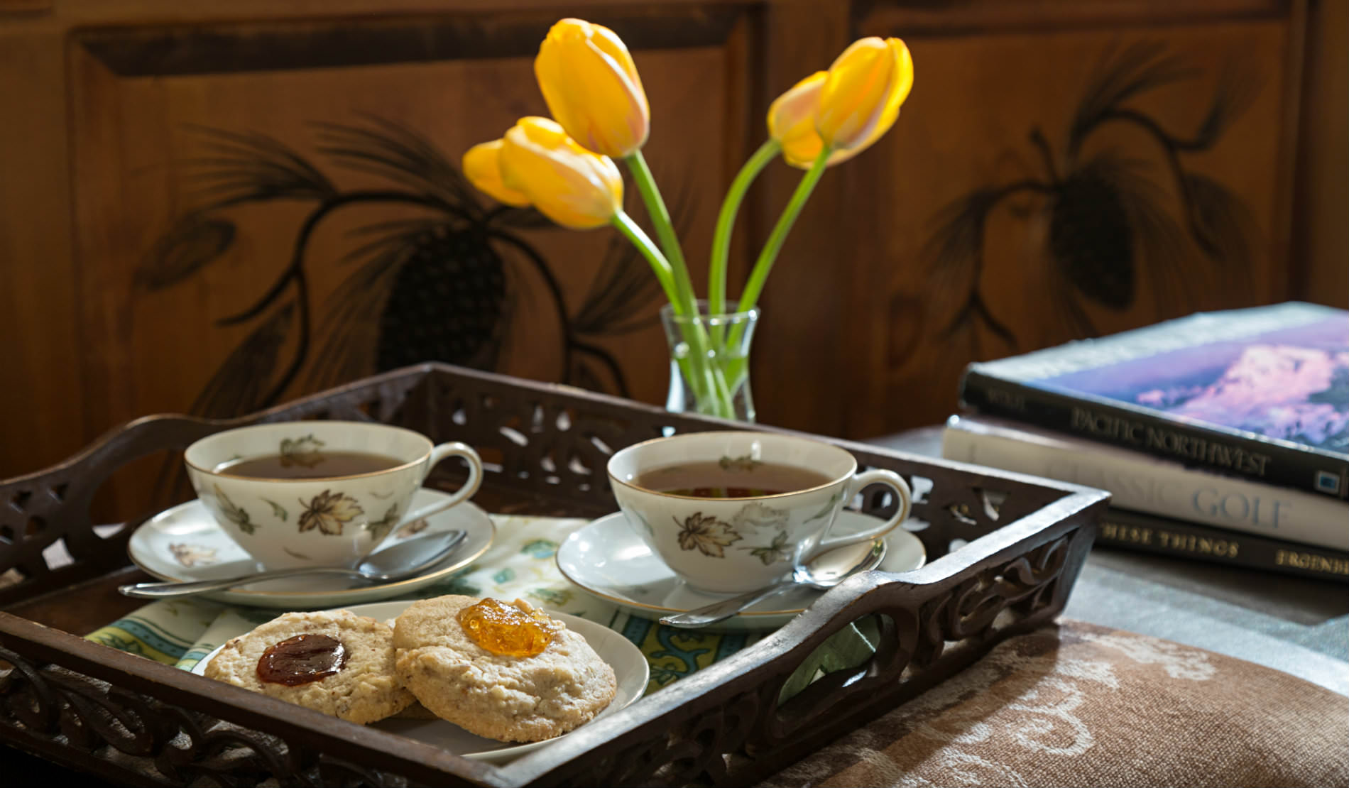 Cookies and tea on wooden server with yellow tulips and stack of books.