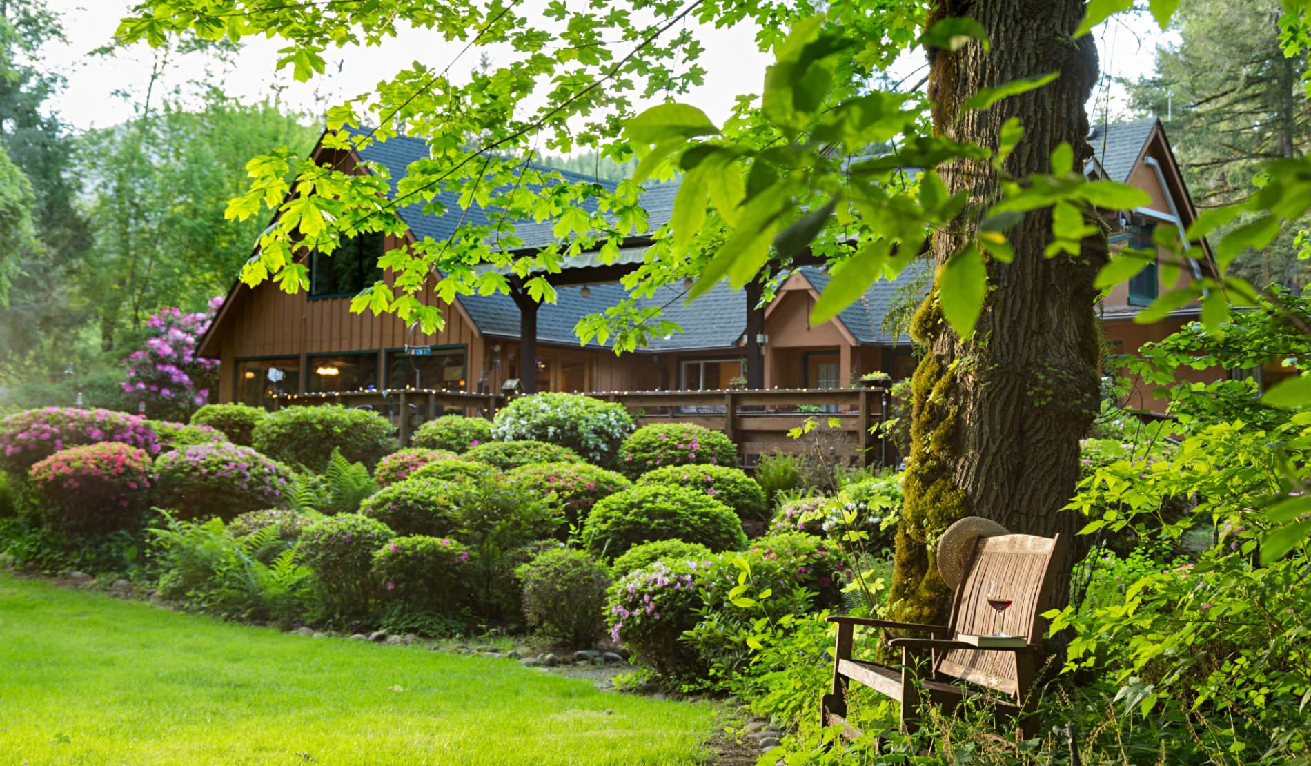 A wooden bench to rest on with blooming red and pink azaleas and the lodge in the background