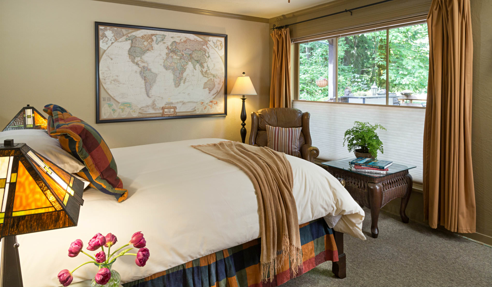 Bed facing large window with view of green trees, map of world, craftsman lamps.