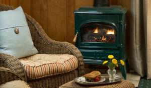 Brown wicker chair with green and patterend cusions in front of wood burning stove