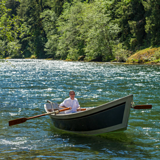 Chef in white coat rowing a rowboat on river sparkling in the sun